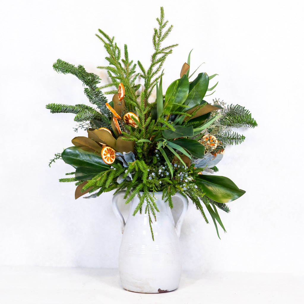 Holiday floral bouquet in a white vase featuring green leaves and orange slice ornaments.