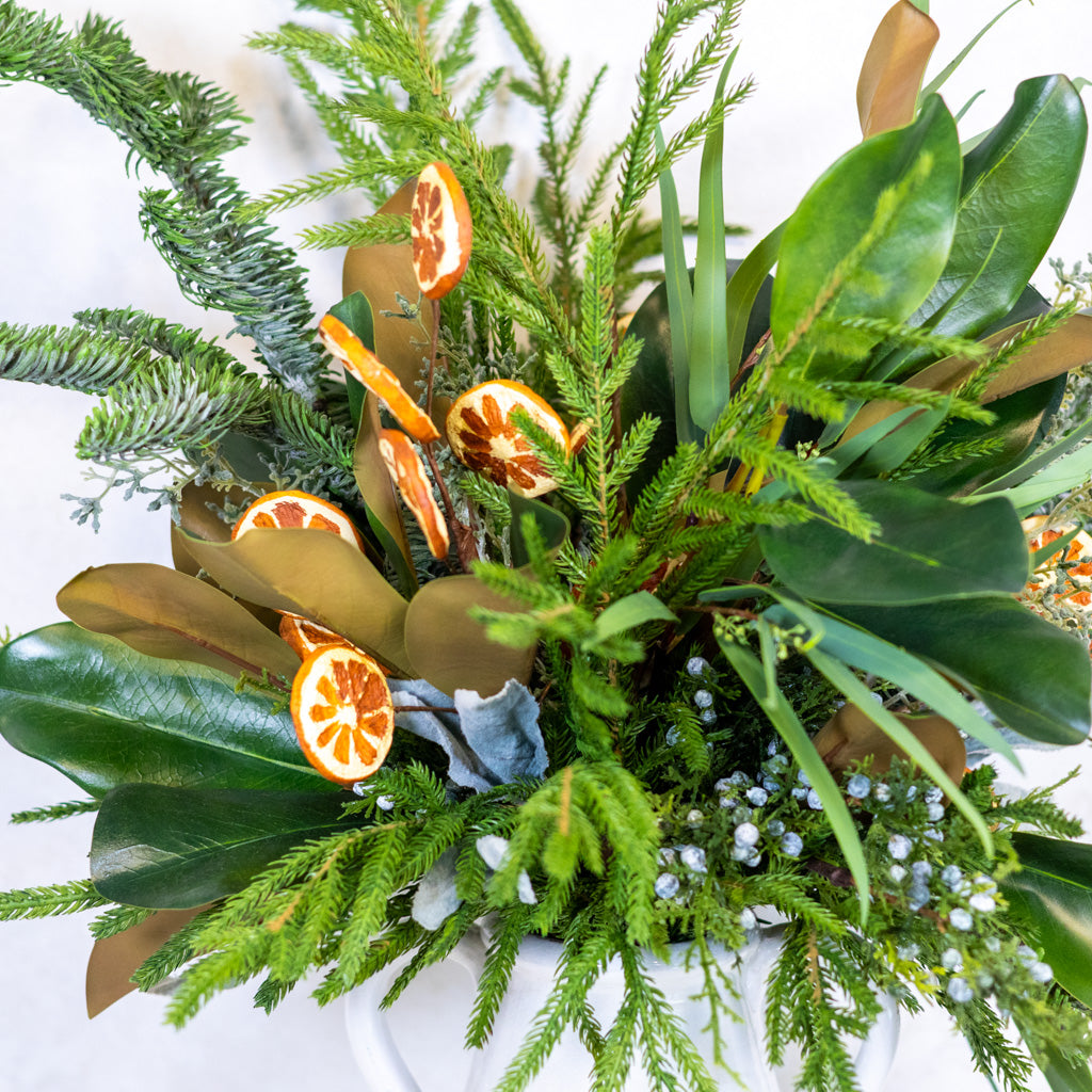 Close-up of holiday bouquet greenery with ribbon, blue fabric, and orange slice accents.