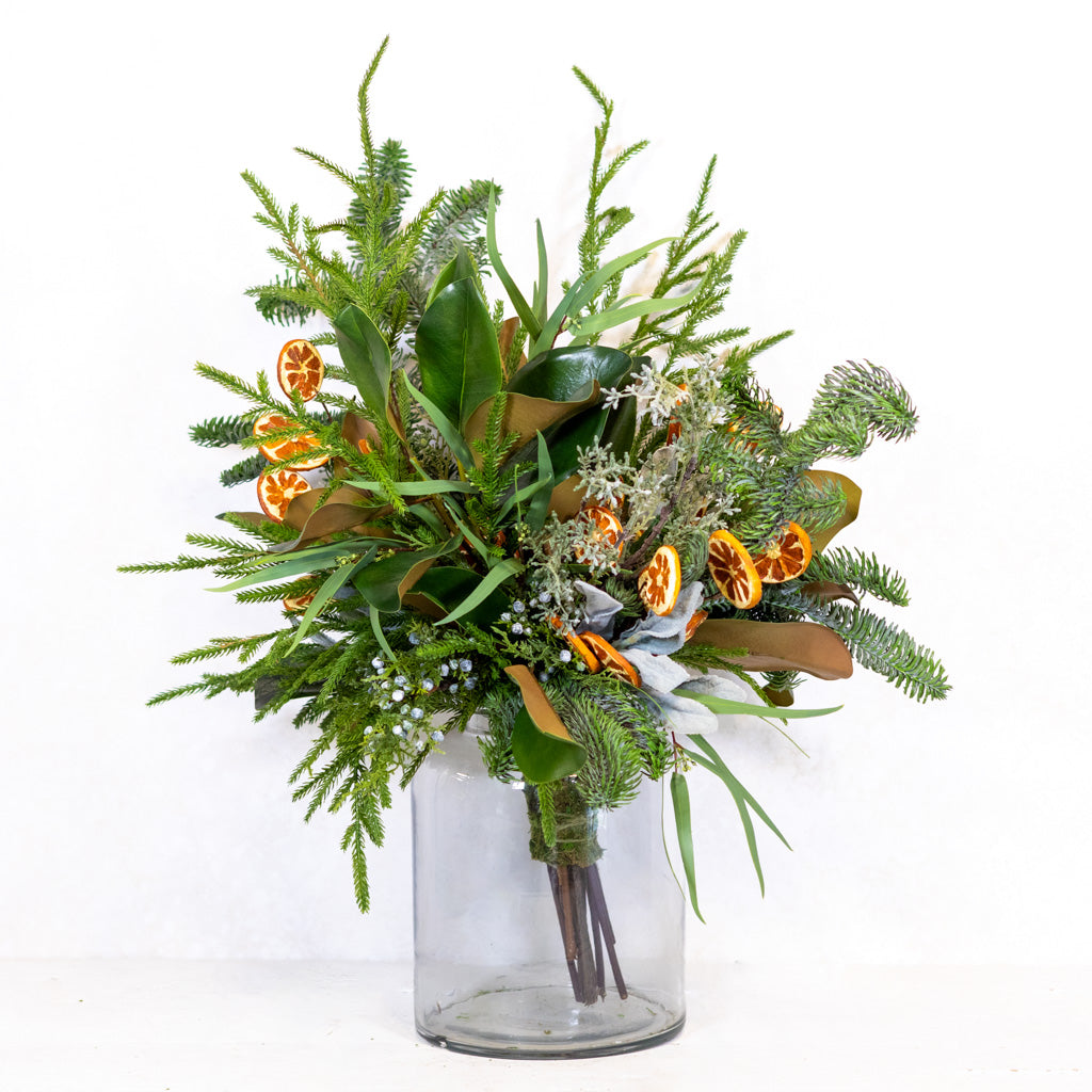 Holiday floral bouquet in a clear vase with green sprigs and orange slice accents.