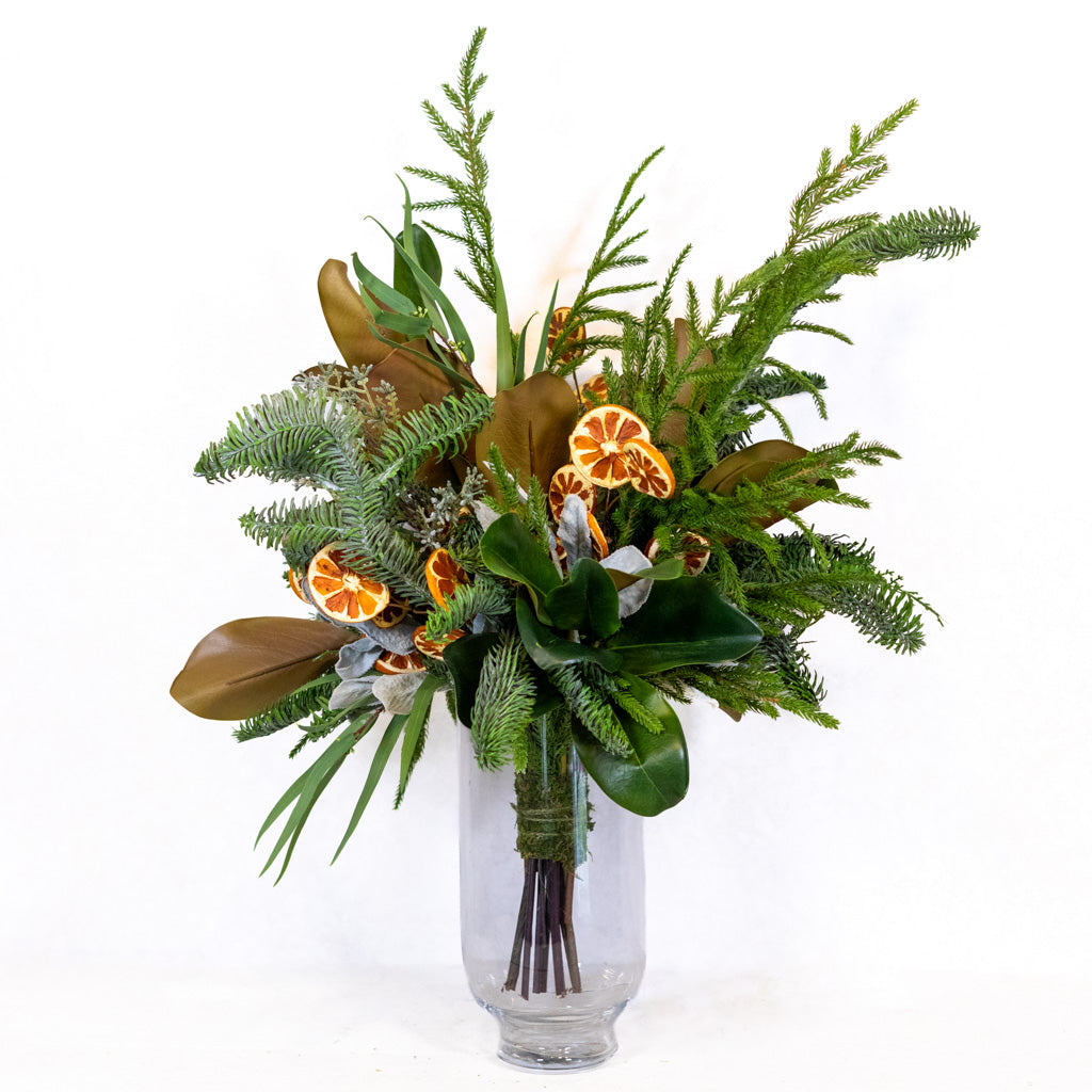 Holiday floral bouquet in a clear vase with green foliage and orange slice ornaments.