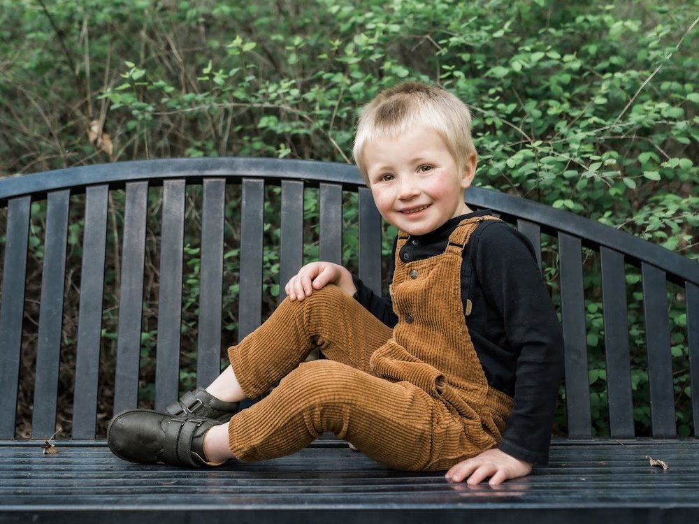 Toddler seated outdoors wearing dark sneakers with strap closures and rubber sole