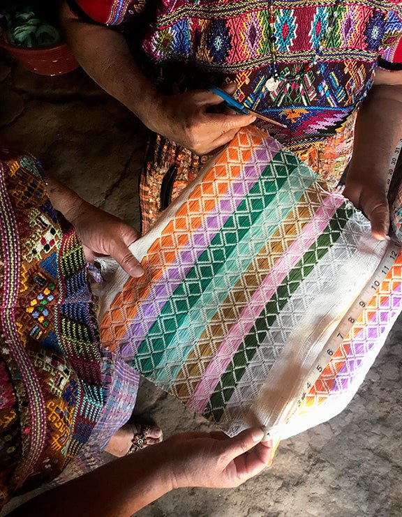 Multi-color geometric pillow cover being folded, with tassel fringe accents at edges