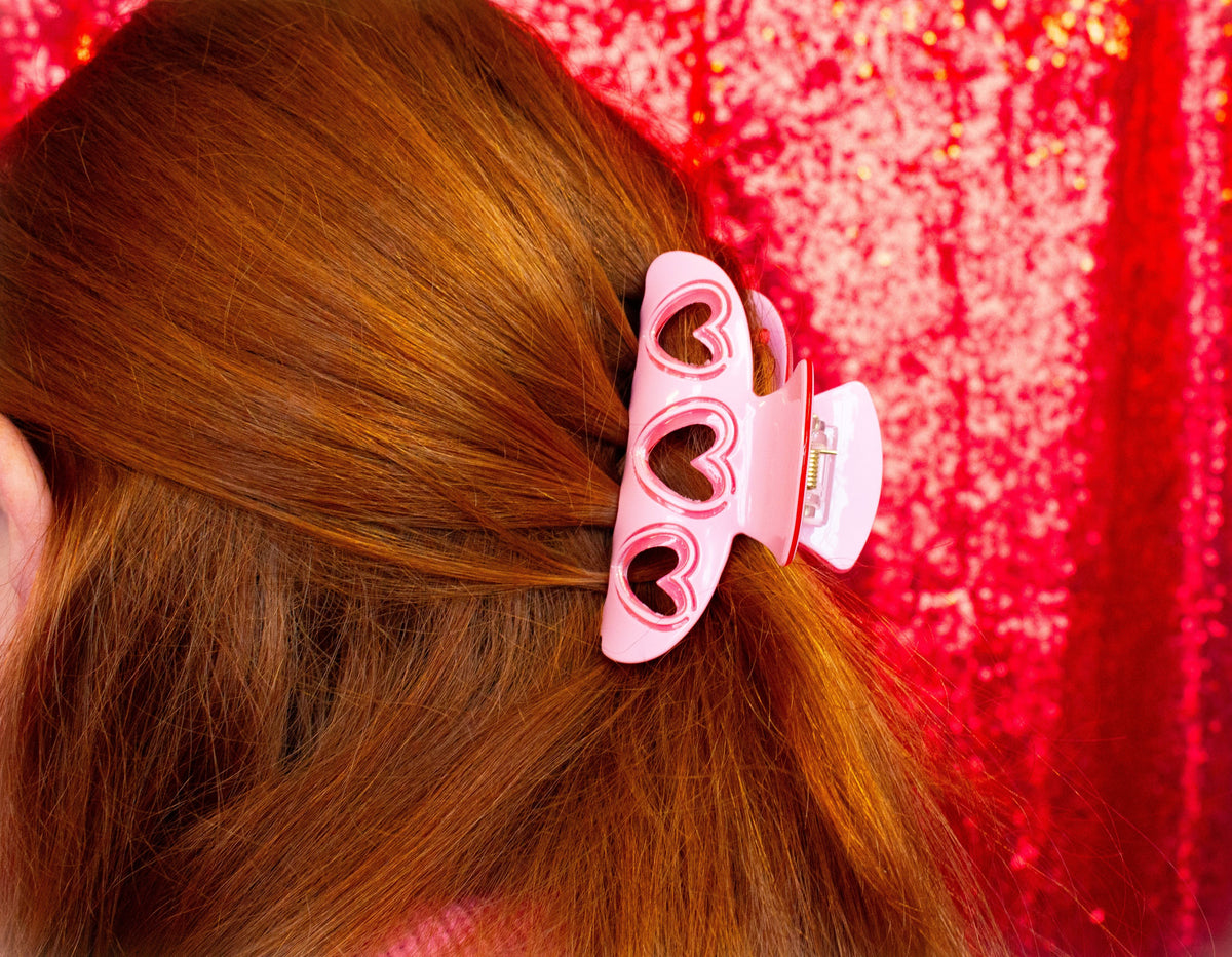 Pink and white heart hair claw with two heart shapes, holding brown hair
