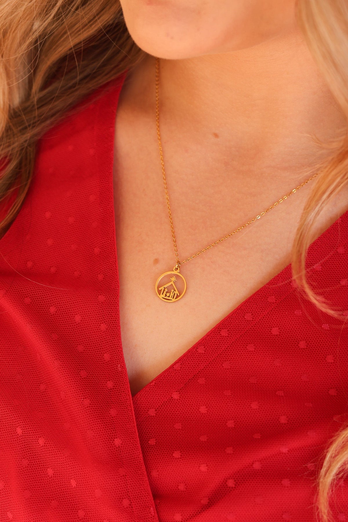 Gold Nativity necklace with round pendant worn over a red dress