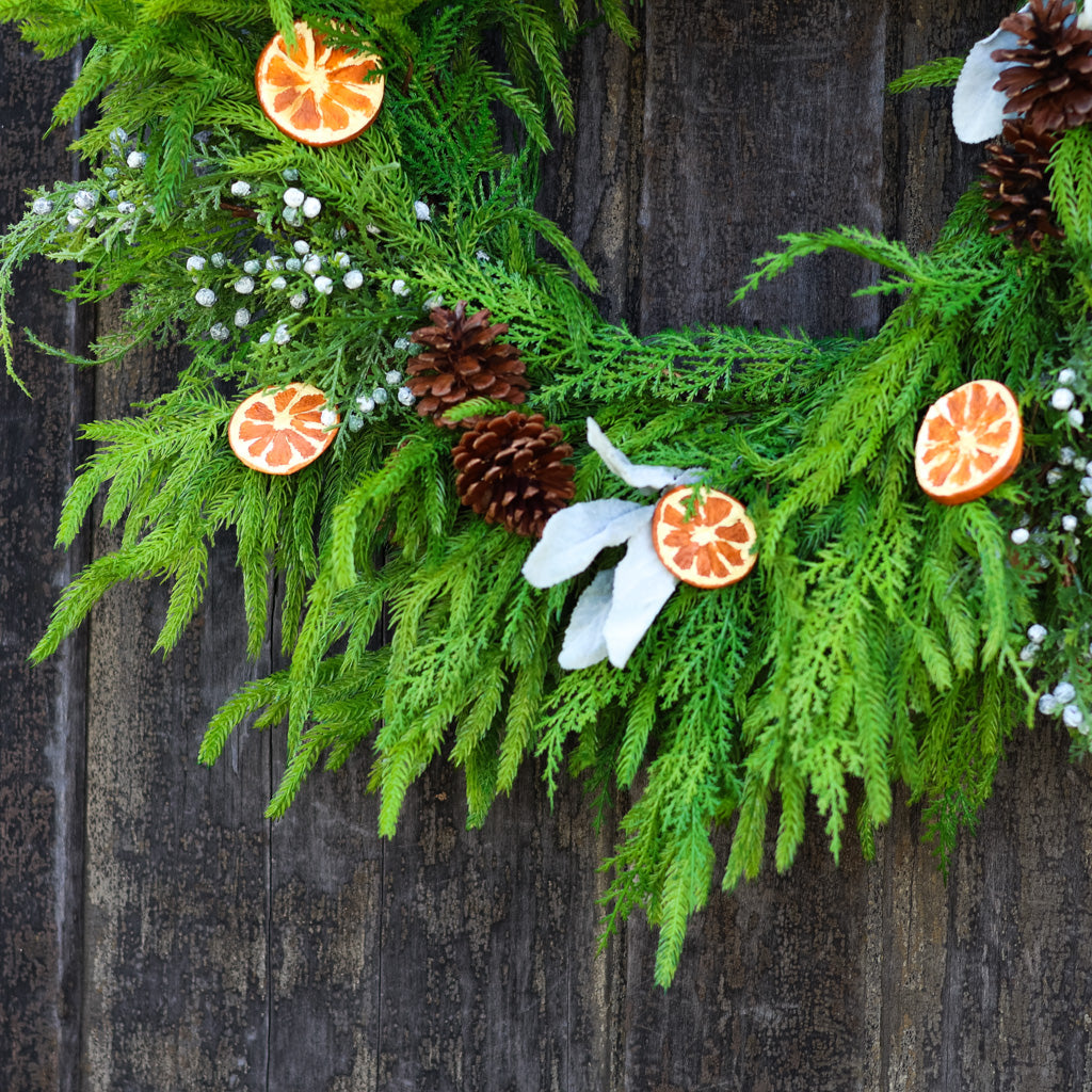 Evergreen wreath with orange slice ornaments, pinecones, and white blossoms on leafy branches