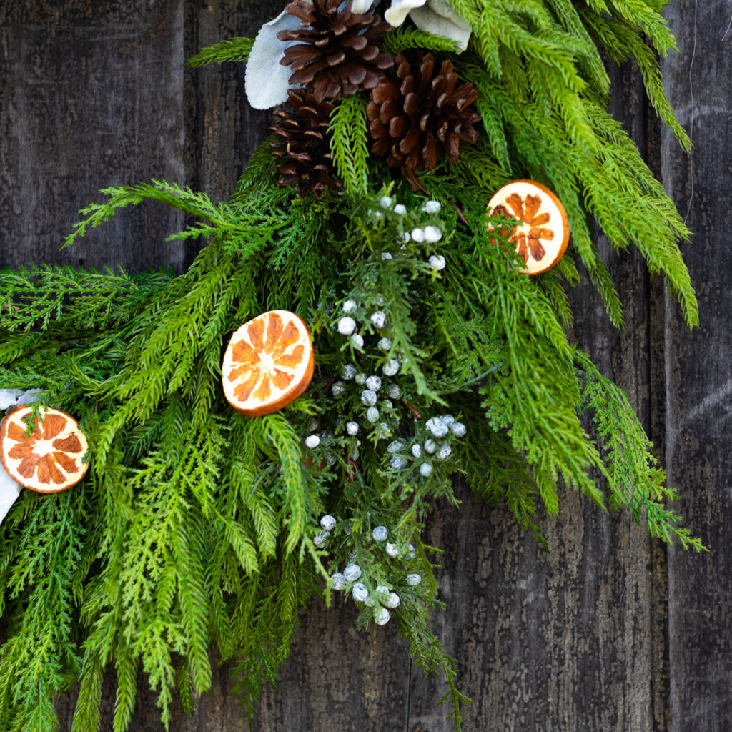 Close-up evergreen wreath with orange slice charm, pinecone cluster, and white berry accents