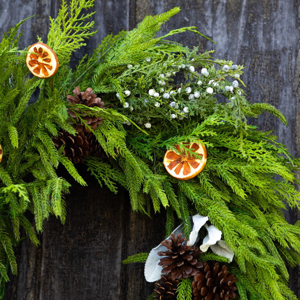 Evergreen wreath detail with orange slice ornaments, pinecones, and small white flower clusters