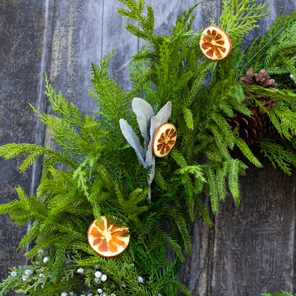 Evergreen wreath corner view with orange slice charms, white blossoms, and pinecone accents