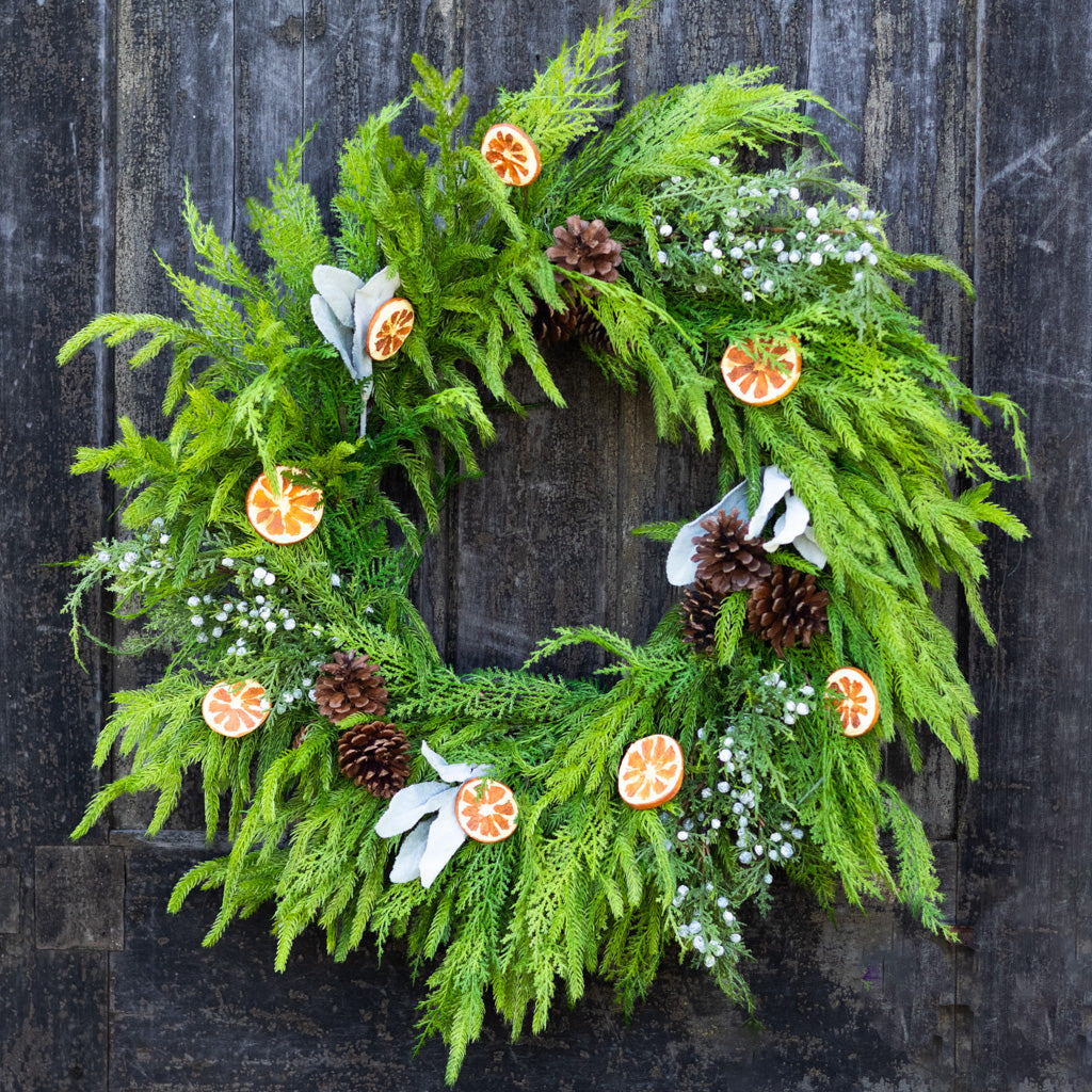 Evergreen wreath with orange slice ornaments, pinecones, white blossoms, and berry clusters