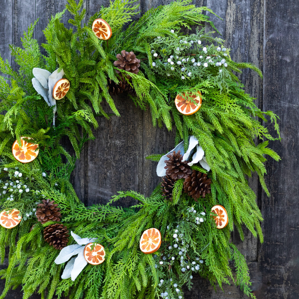 Decorative evergreen wreath with orange slices, pinecones, white flowers, and dangling greenery