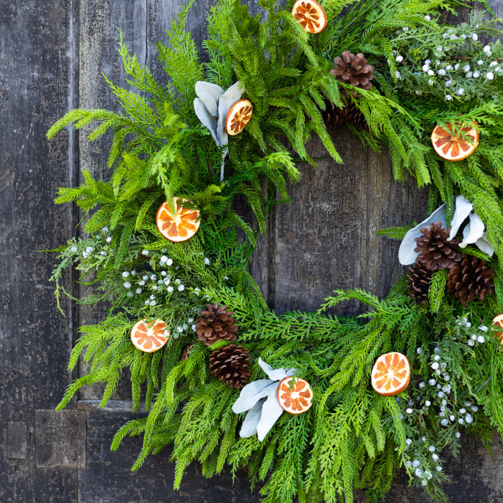 Evergreen holiday wreath featuring orange slice charms, pinecones, and white berry blossoms