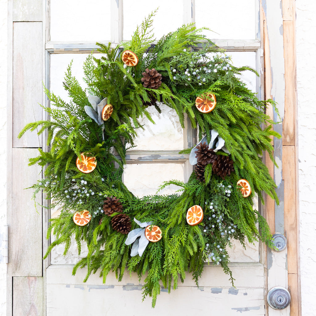 Evergreen wreath with orange slice decorations, pinecones, white blossoms, and berry garland