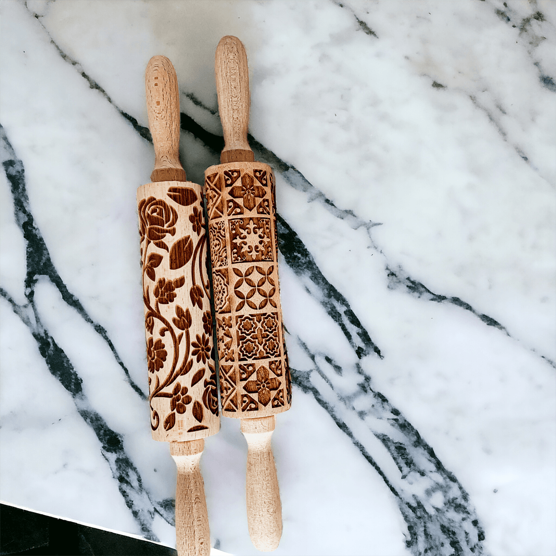Two embossed wood rolling pins with floral and geometric carving on marble surface