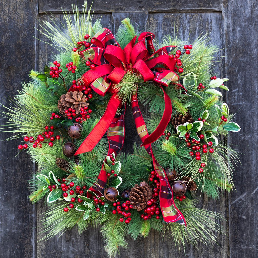 Holiday wreath with red plaid ribbon, pine greenery, pinecones, berries, and bell accents