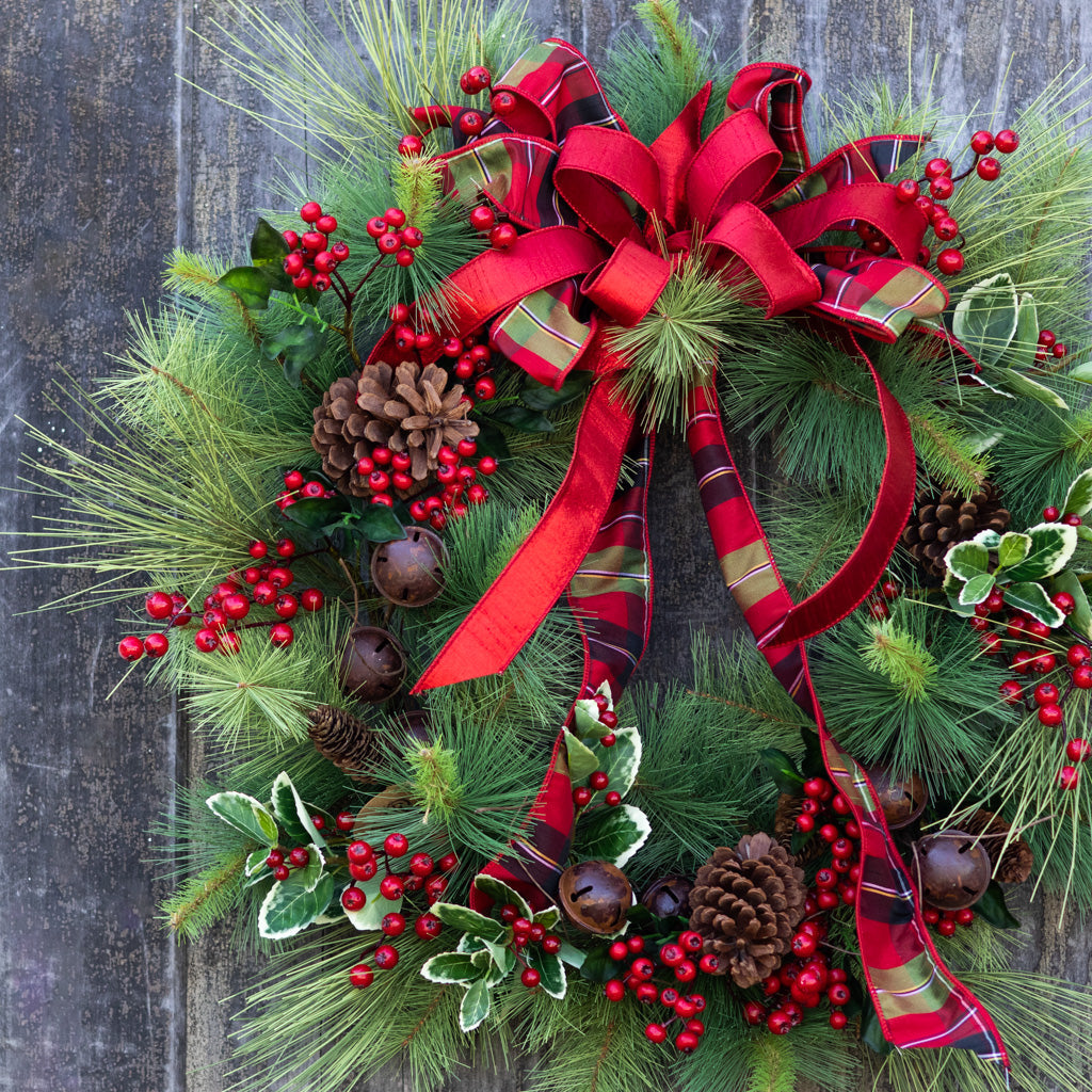 Holiday wreath detail with red plaid ribbon, evergreen needles, berry clusters, pinecones, bells