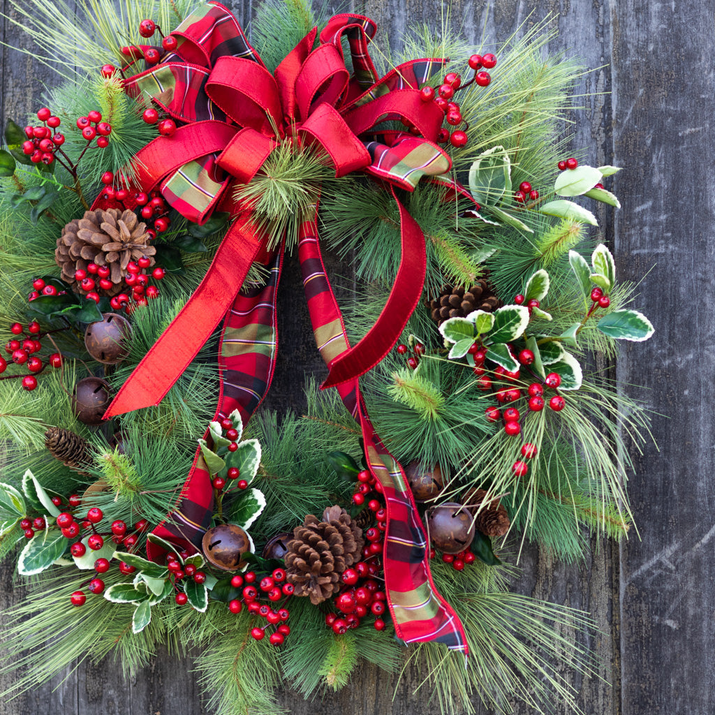 Holiday wreath with large red plaid bow, pine greenery, pinecones, red berries, and bells