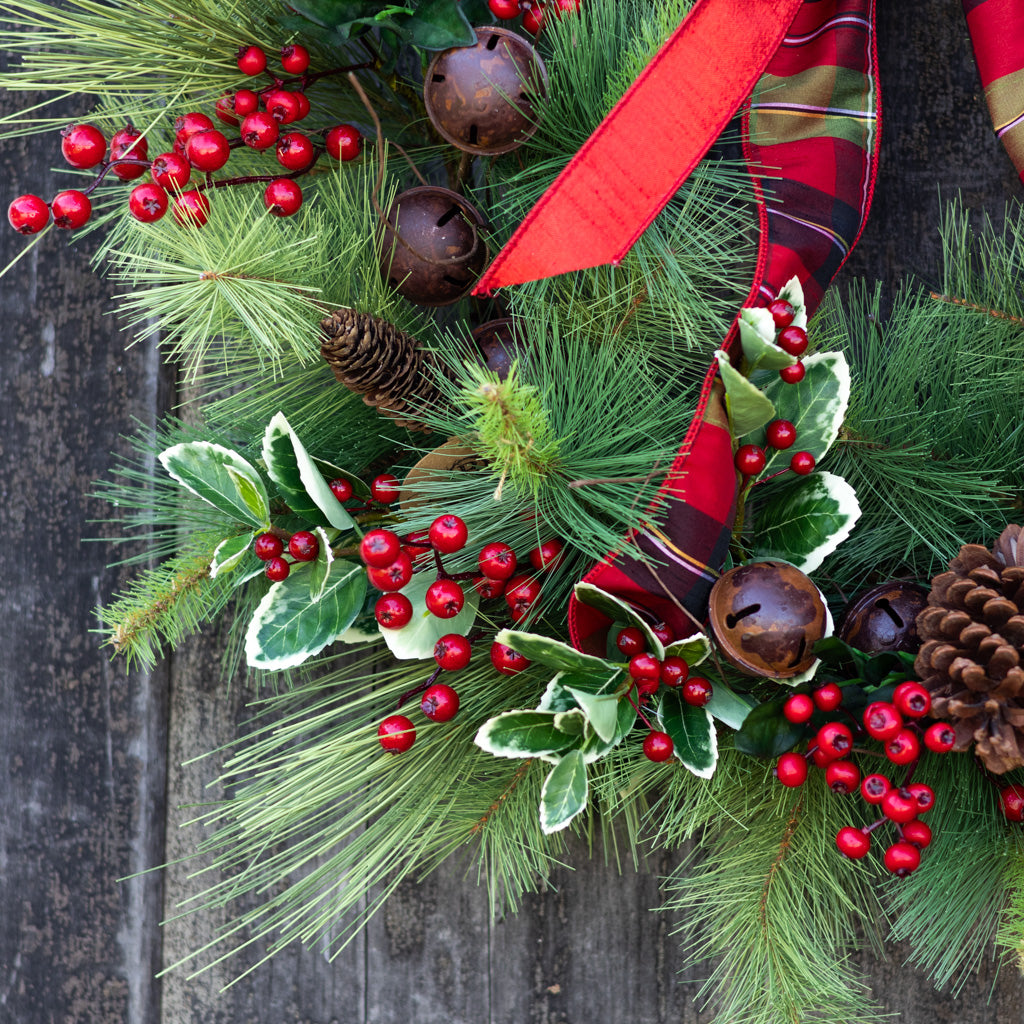 Holiday wreath with pine needles, red berries, pinecones, brown bells, and white-edged leaves