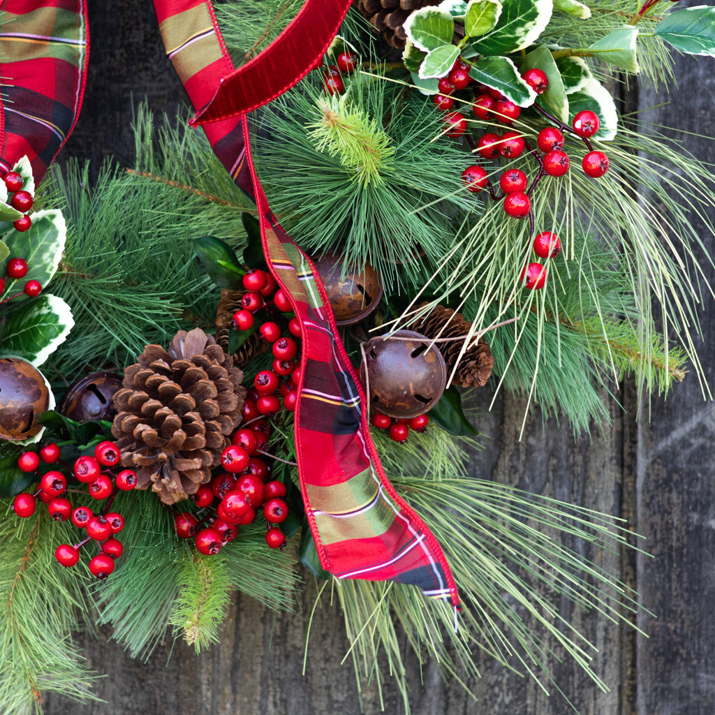 Holiday wreath close-up with red plaid ribbon, evergreen sprigs, red berries, and bells