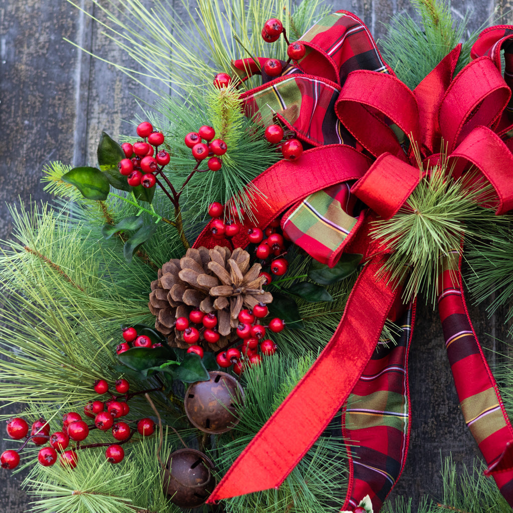 Holiday wreath with red ribbon, pine needles, red berries, pinecones, and brown bell ornaments