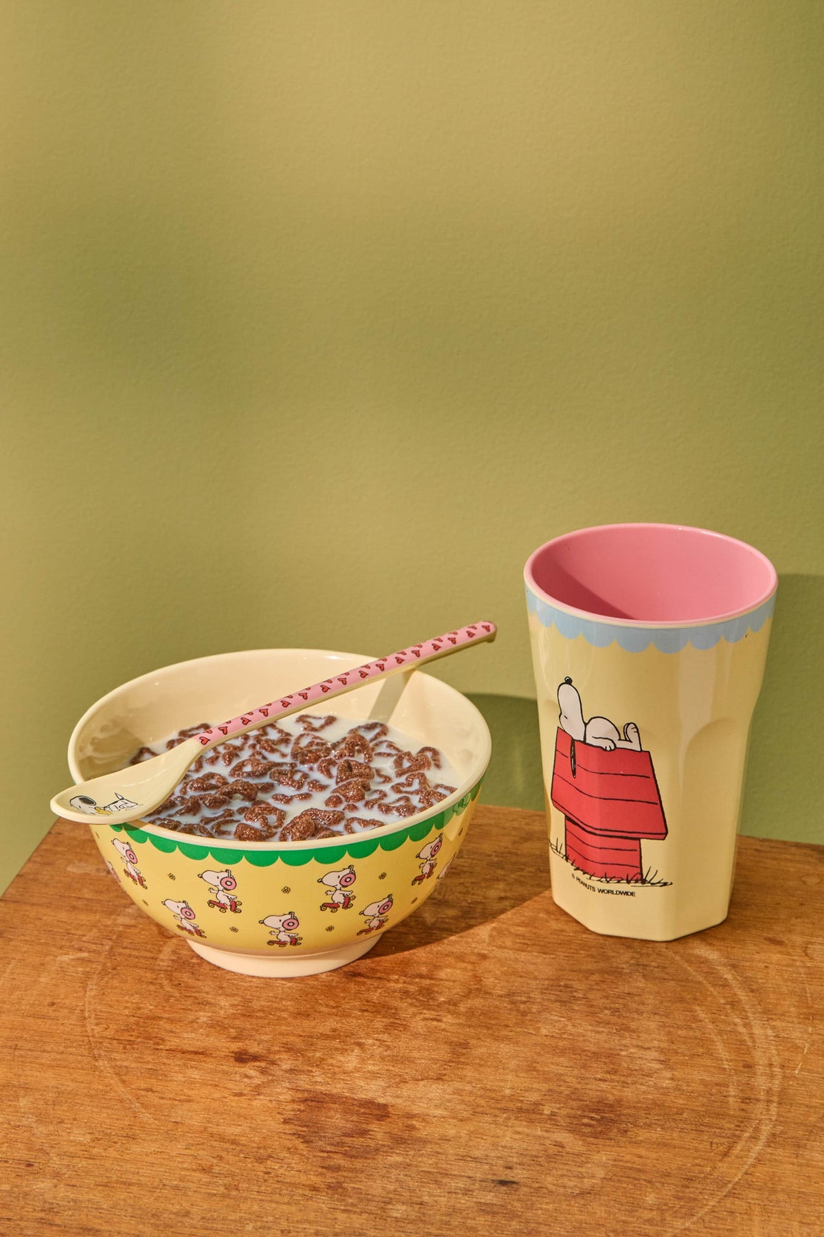 Snoopy melamine latte spoon with pink striped handle, resting in patterned bowl