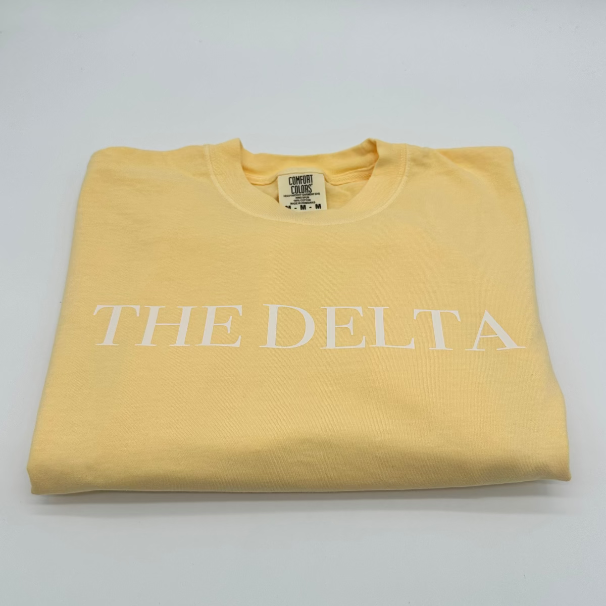 Butter yellow crew-neck graphic T-shirt with white “THE DELTA” text on the chest.