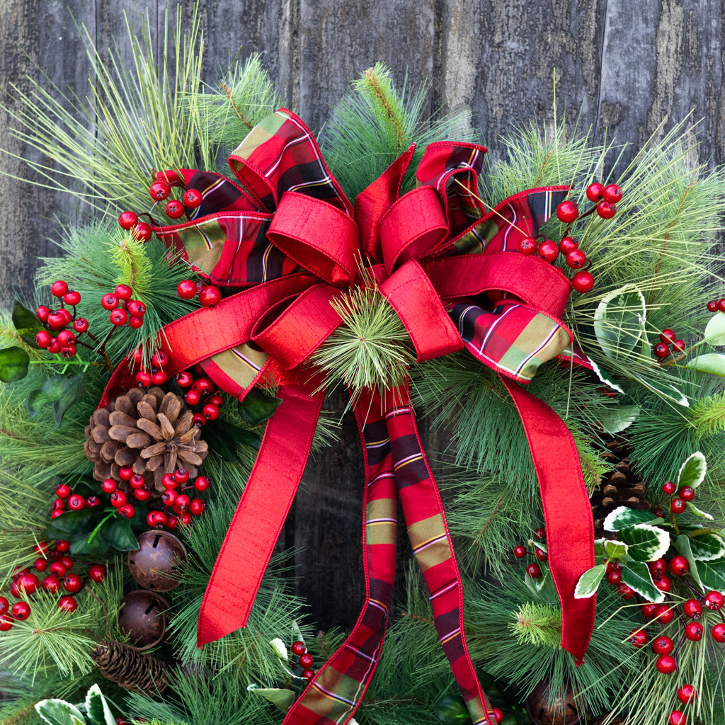 Holiday wreath with red plaid bow, evergreen foliage, red berries, pinecones, and bell accents