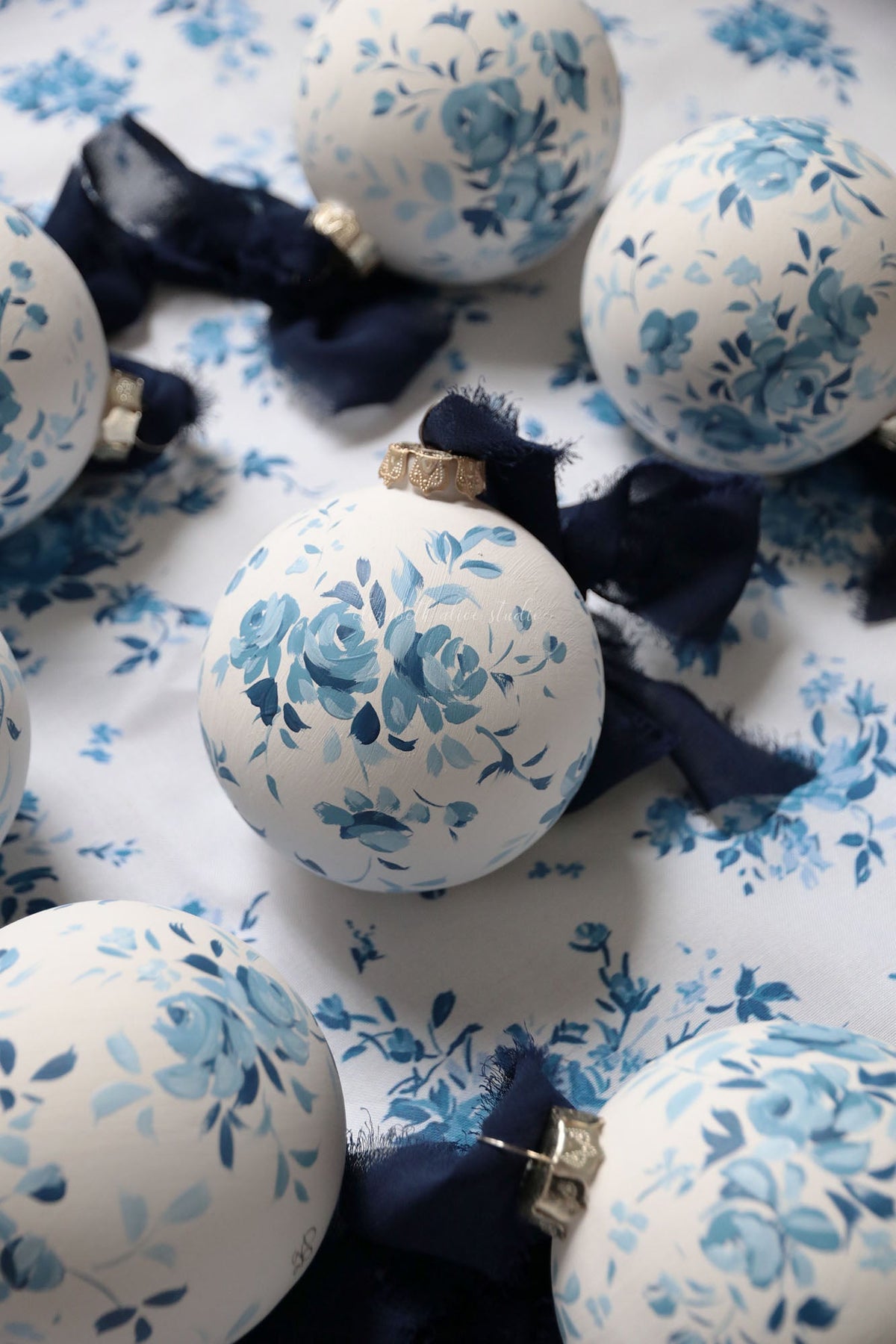 Close-up of a white ornament with hand-painted blue roses and a navy bow