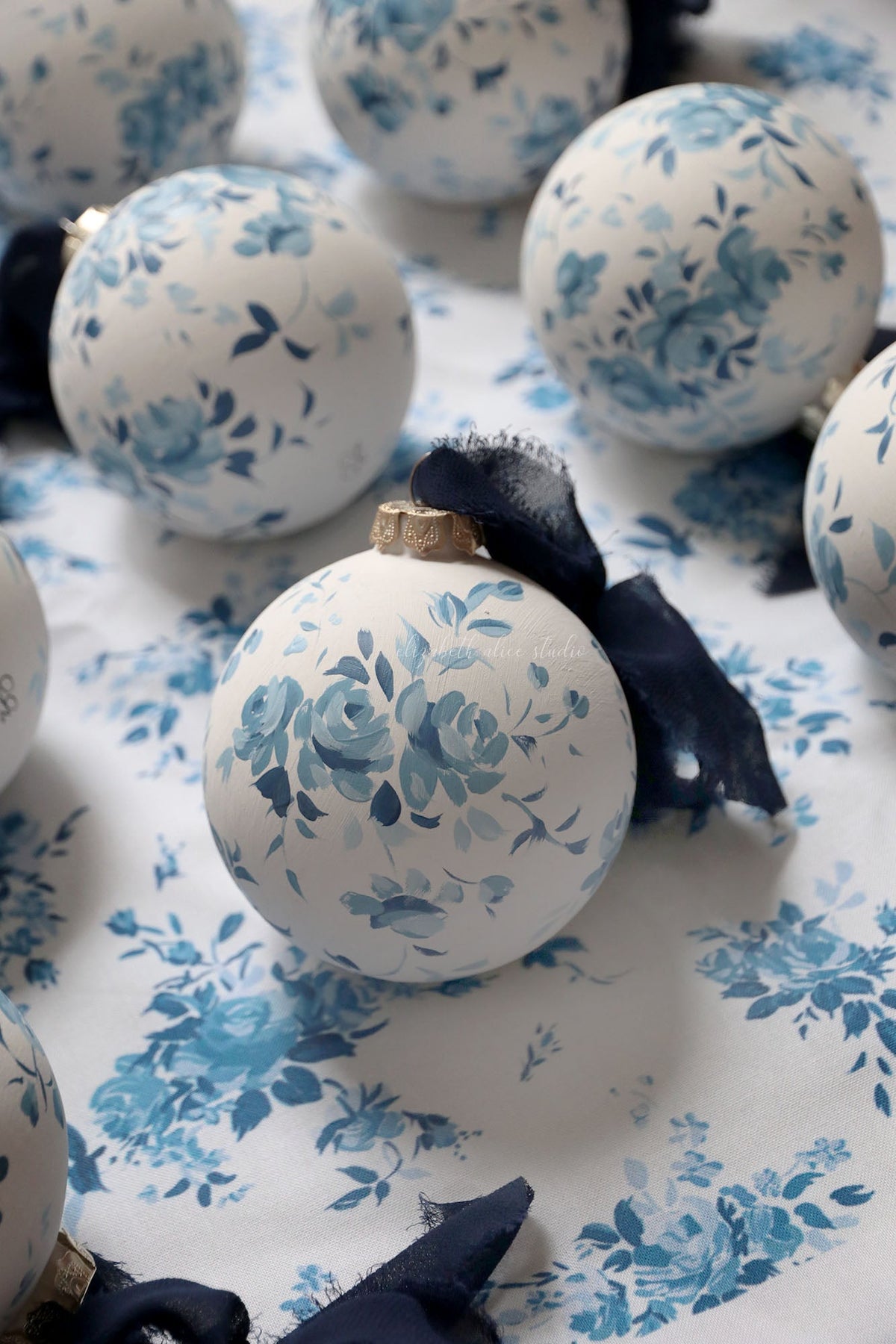White ornament featuring hand-painted blue roses and a navy fabric bow