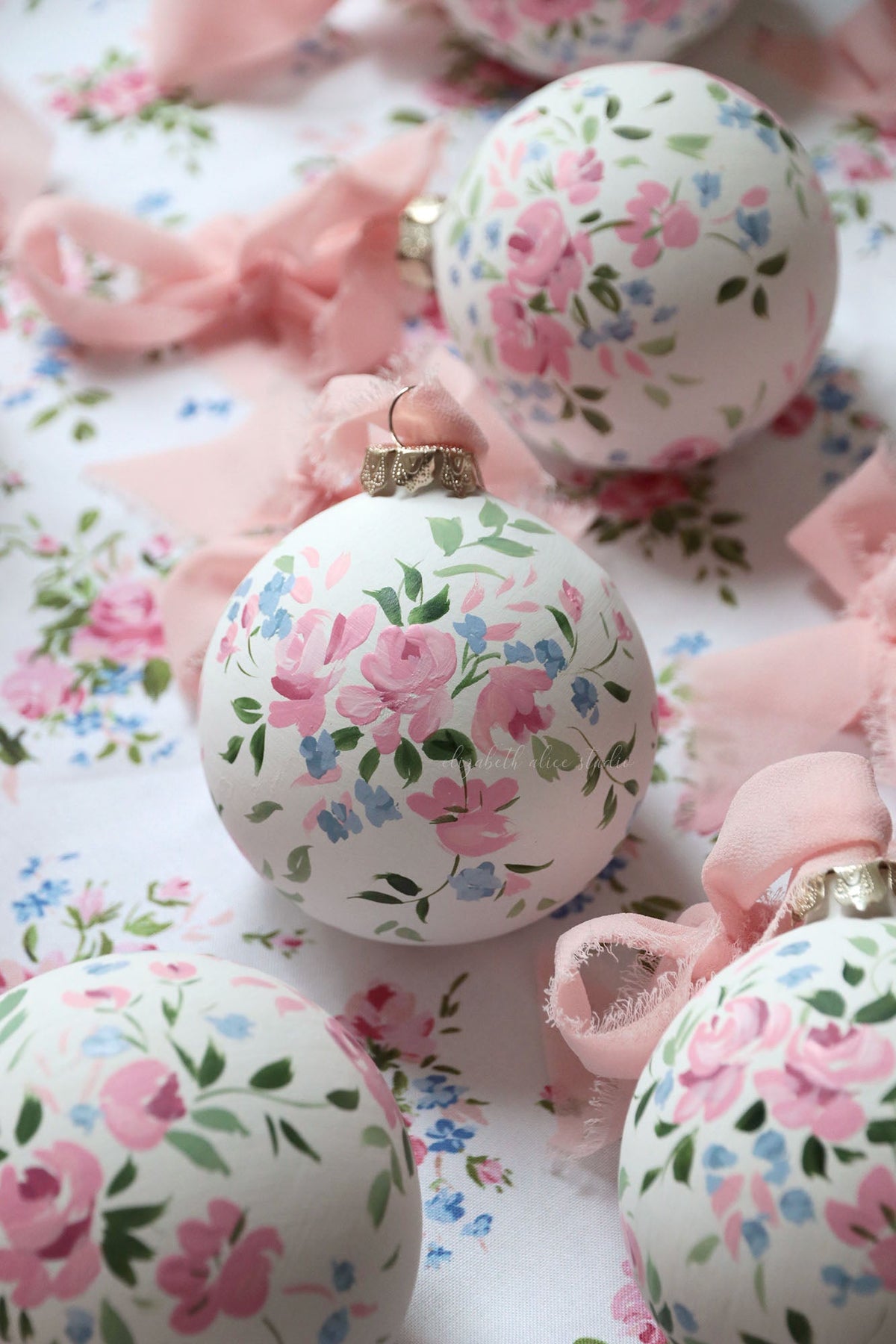 White hanging ornament decorated with pink roses, blue blossoms, and green leaves