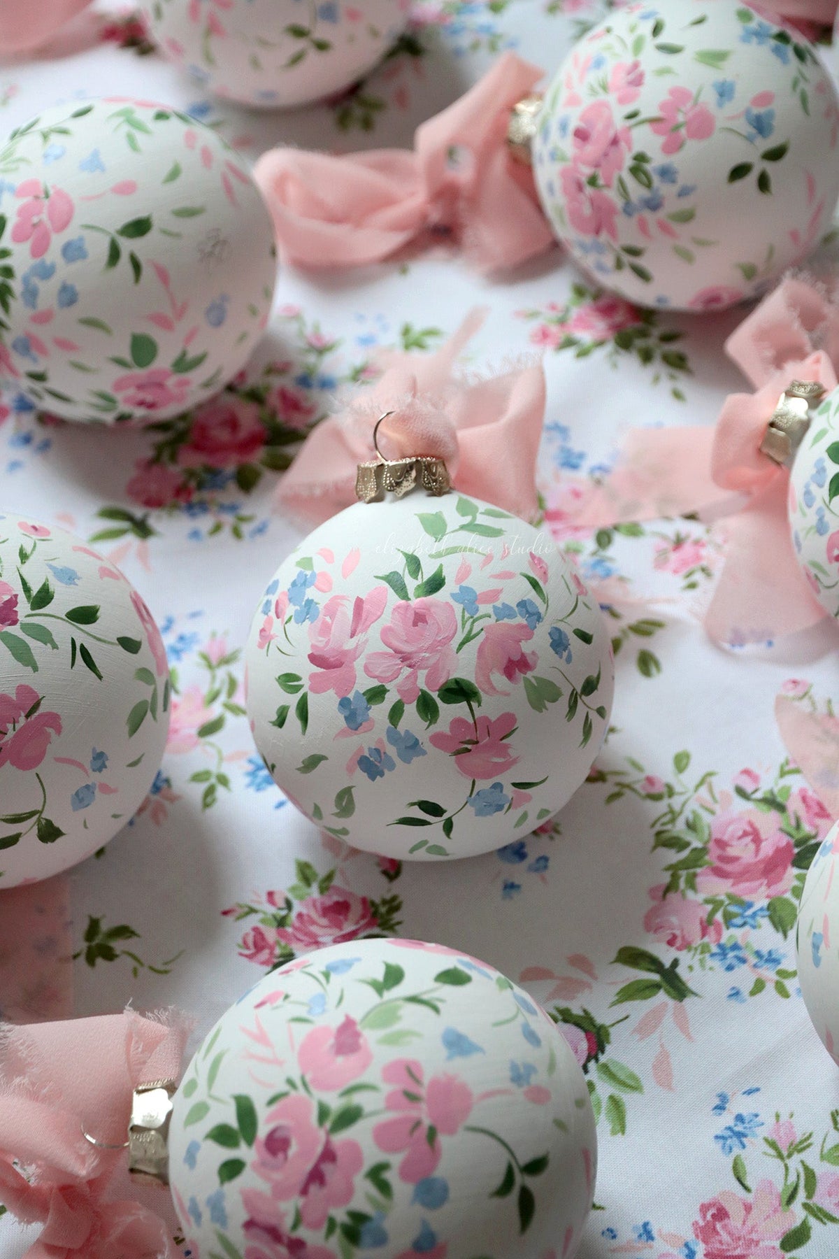 White Christmas ornament with hand-painted pink roses, green leaves, and metal hanging cap