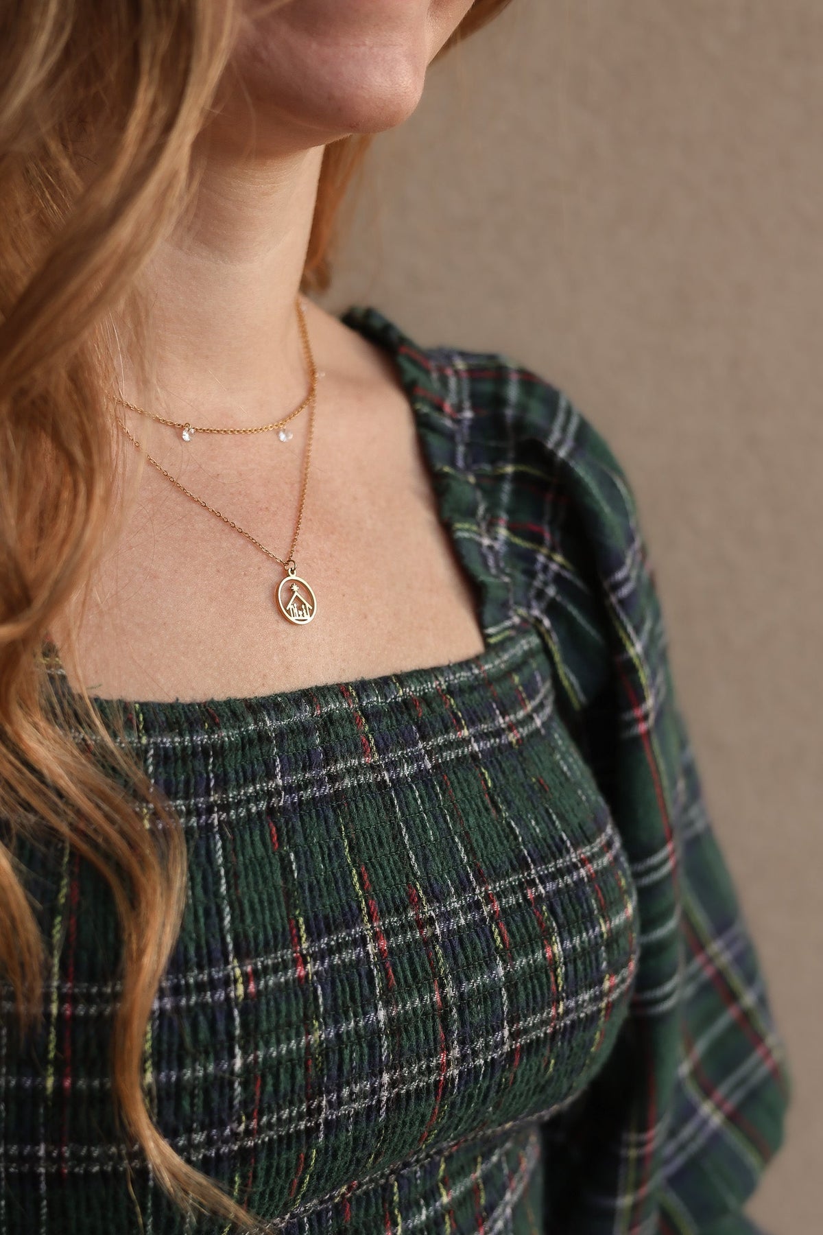 Gold Nativity necklace worn over a green plaid top