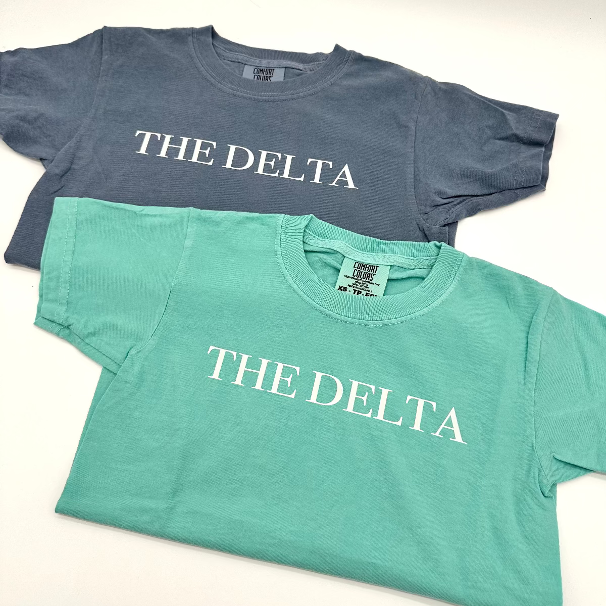 Teal and blue-wash youth tees with 'THE DELTA' front print