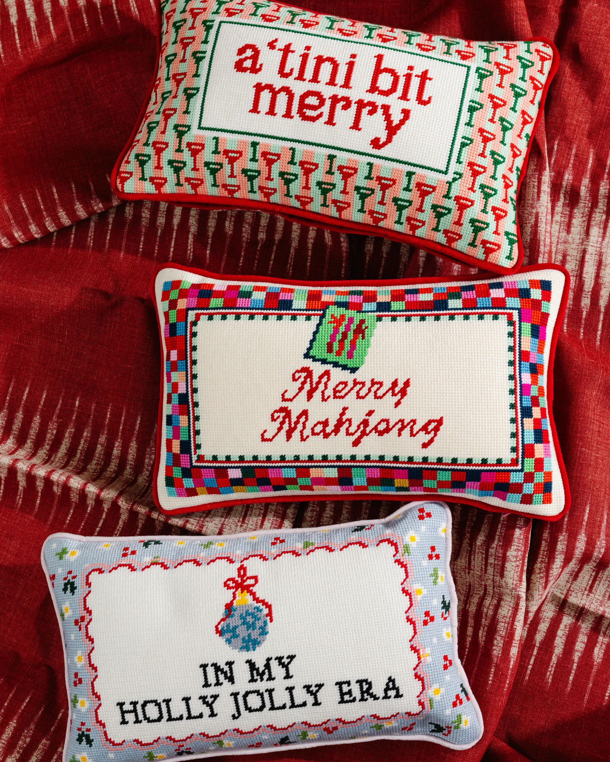 Rectangular needlepoint pillow with 'IN MY HOLLY JOLLY ERA' on a red upholstered seat