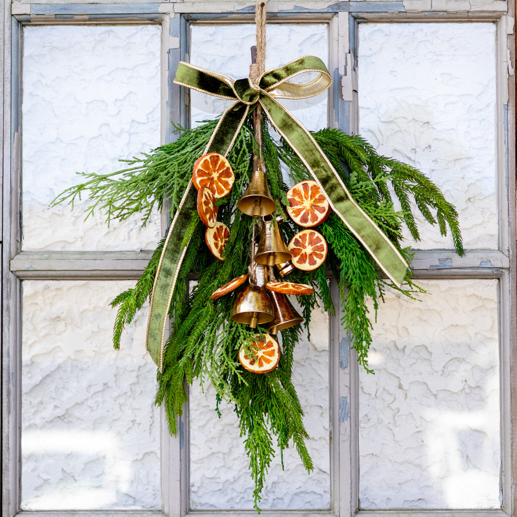 Hanging pine wreath with green ribbon and gold bells, orange slice ornaments