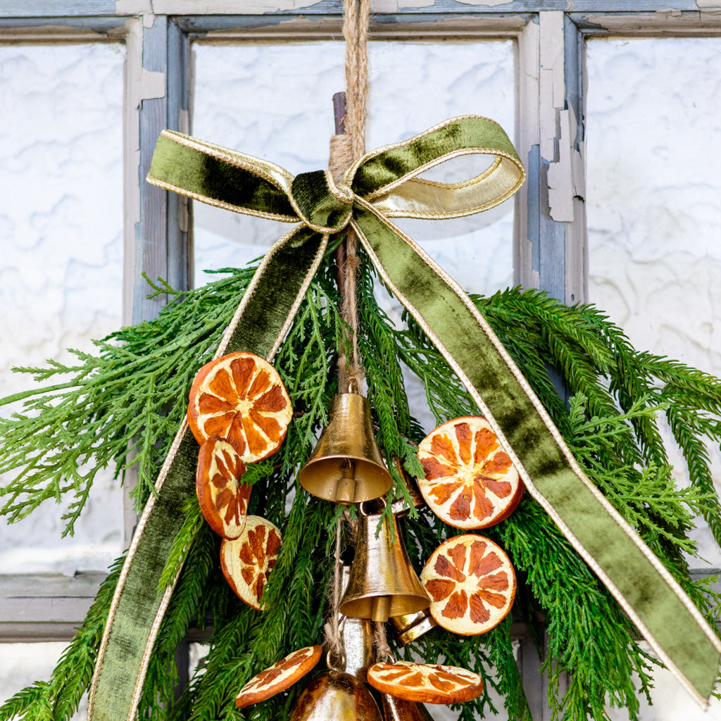 Hanging pine wreath with gold bells and orange slice ornaments, green ribbon bow