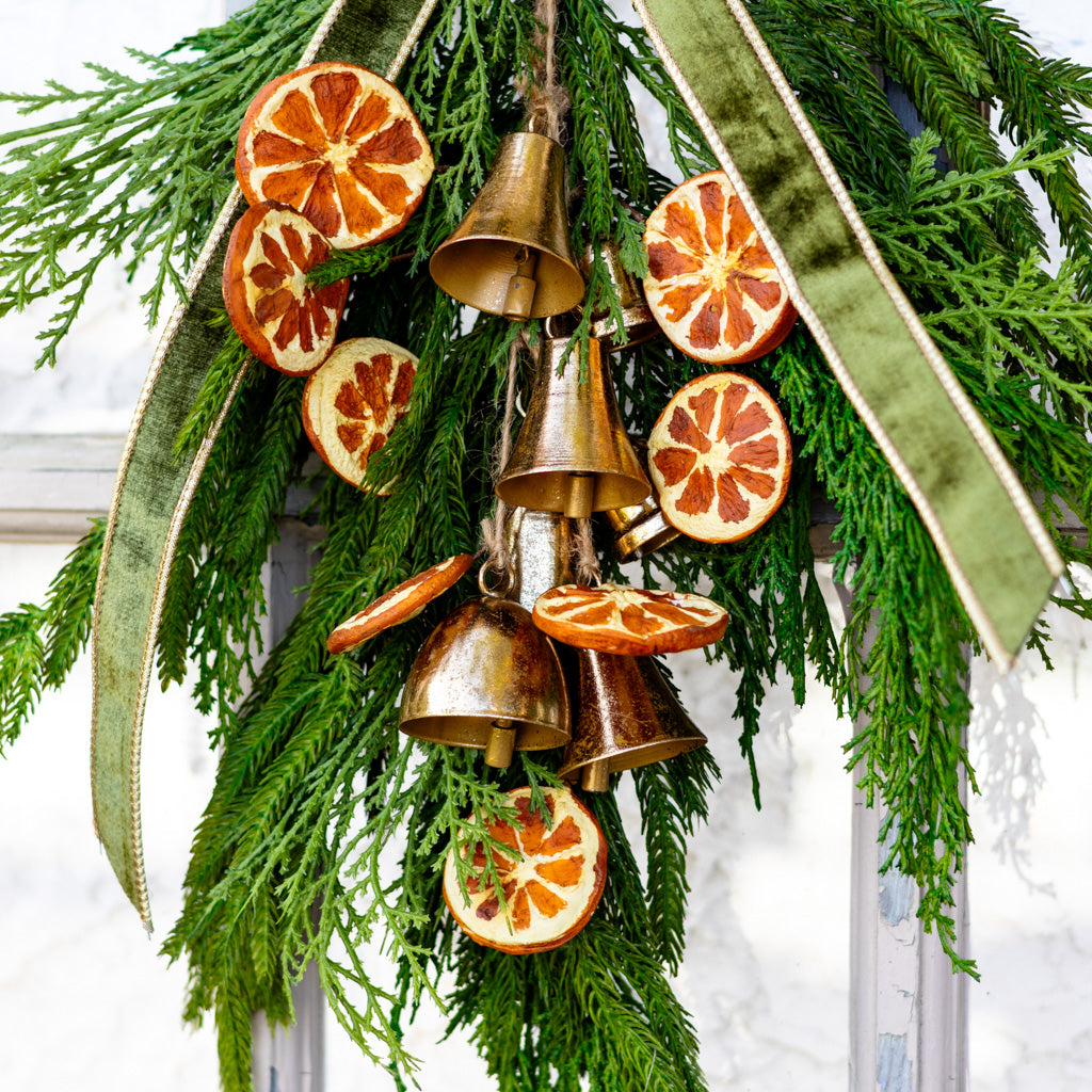 Close-up hanging pine wreath with gold bells and orange slice decorations