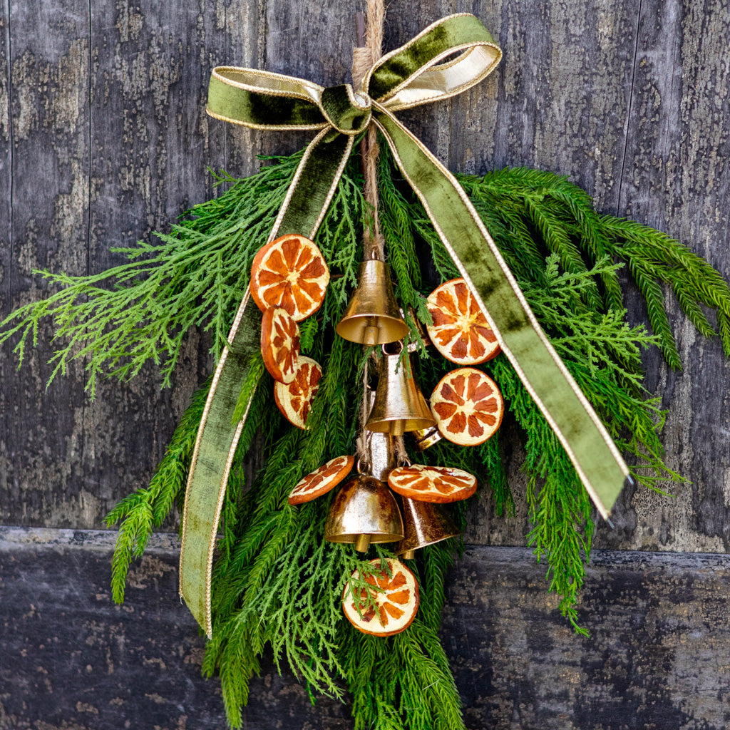 Hanging pine wreath decoration with gold bells, orange slices, and green ribbon streamers