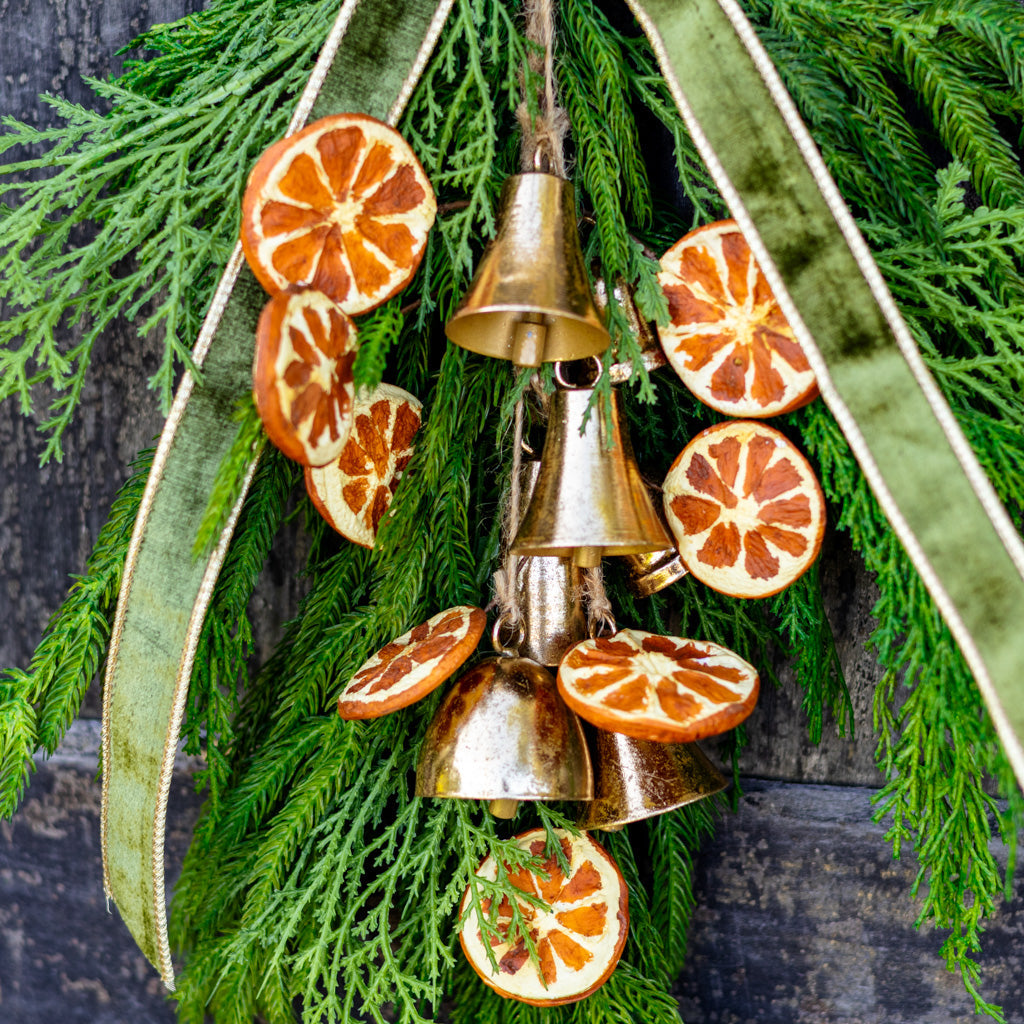 Close-up of hanging pine wreath bells with orange slice ornaments and green ribbon