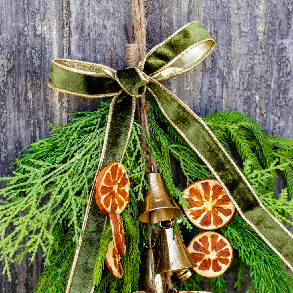 Hanging pine wreath with gold bells and orange slice ornaments, green ribbon loops