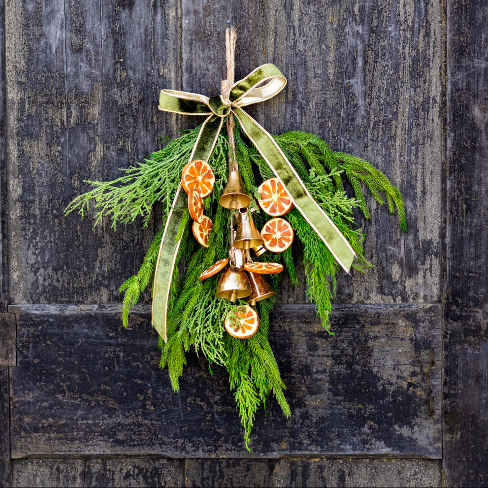 Hanging pine wreath with gold bells and orange slice decorations, tied with green bows