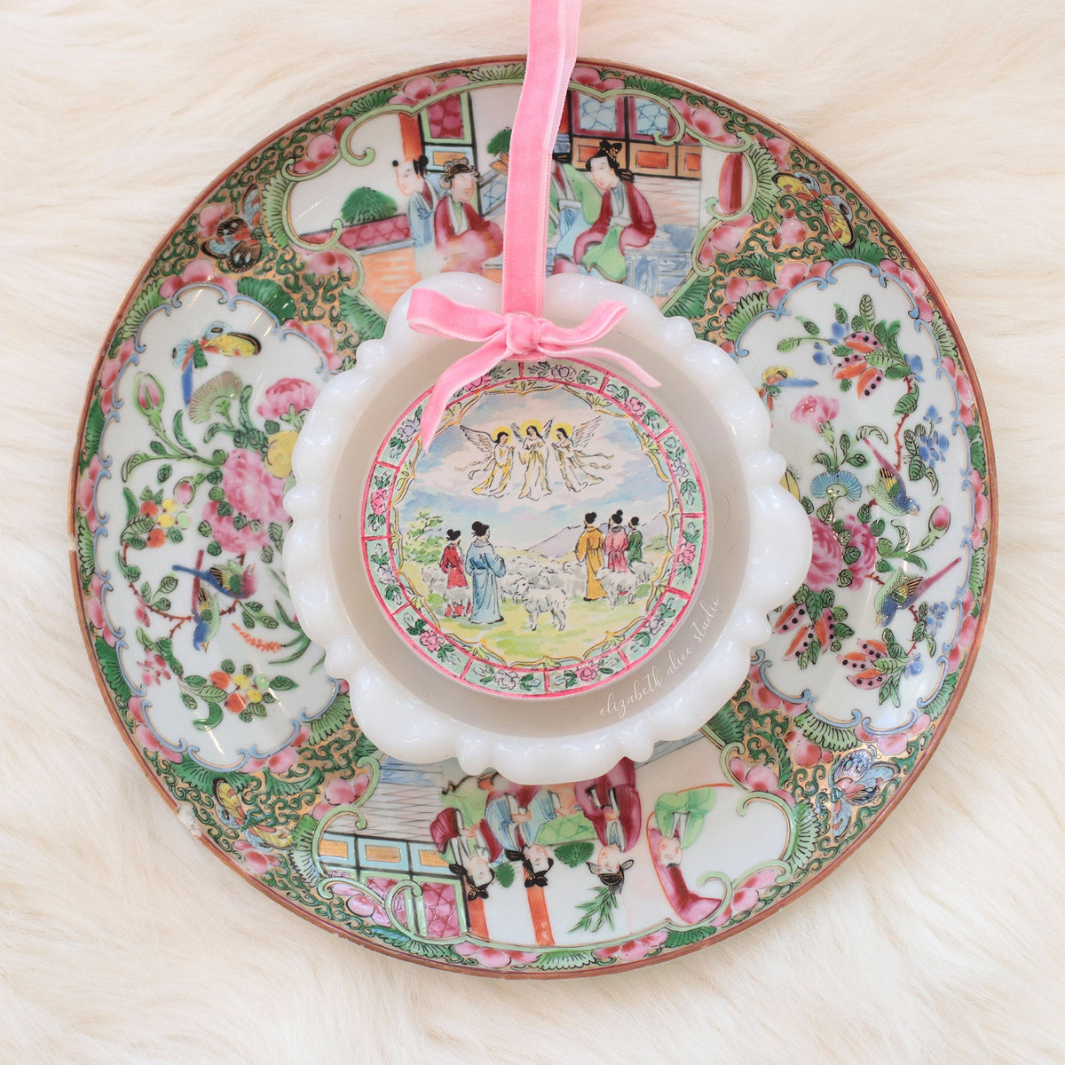 Scalloped acrylic ornament with shepherds and angels scene and pink ribbon on a decorative plate
