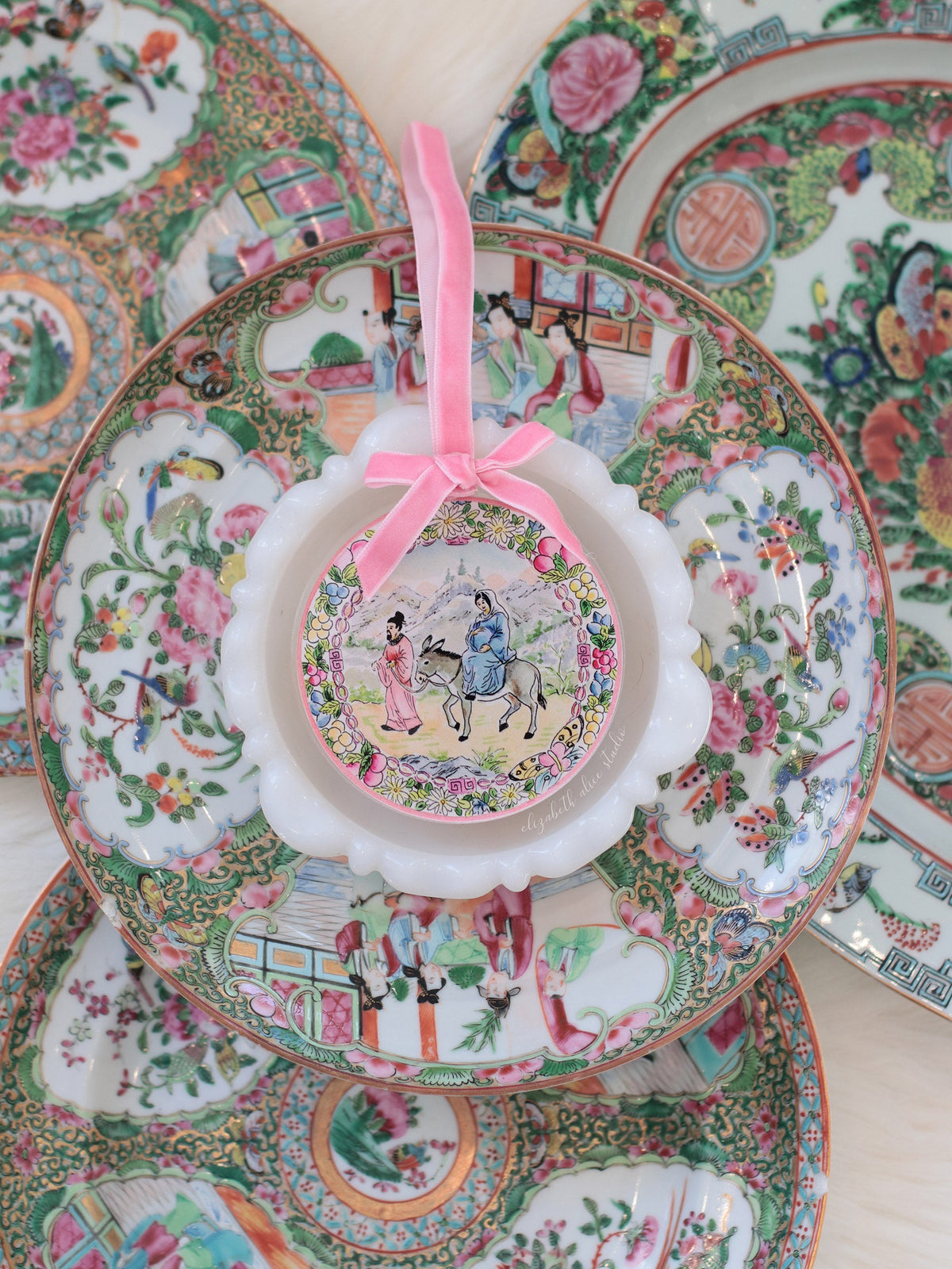 Round acrylic ornament with scalloped white edge, pink bow and Bethlehem journey scene