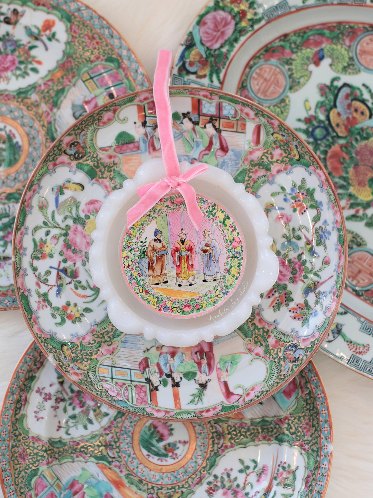 Magi ornament with pink bow, shown against decorative floral plates