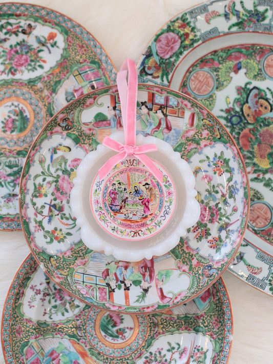 Small round temple scene ornament with pink bow, displayed against decorative plates