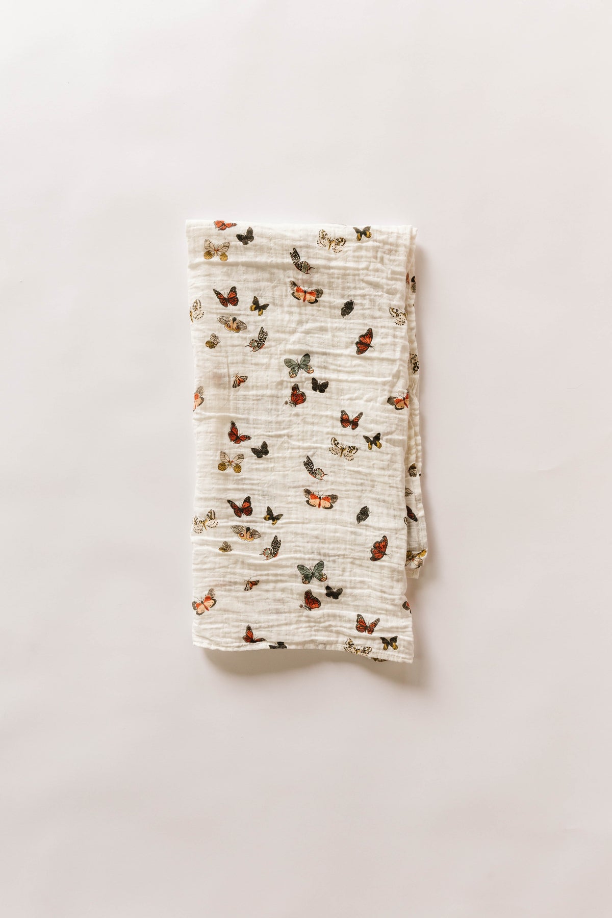 Folded white muslin swaddle blanket with small multicolor butterfly print