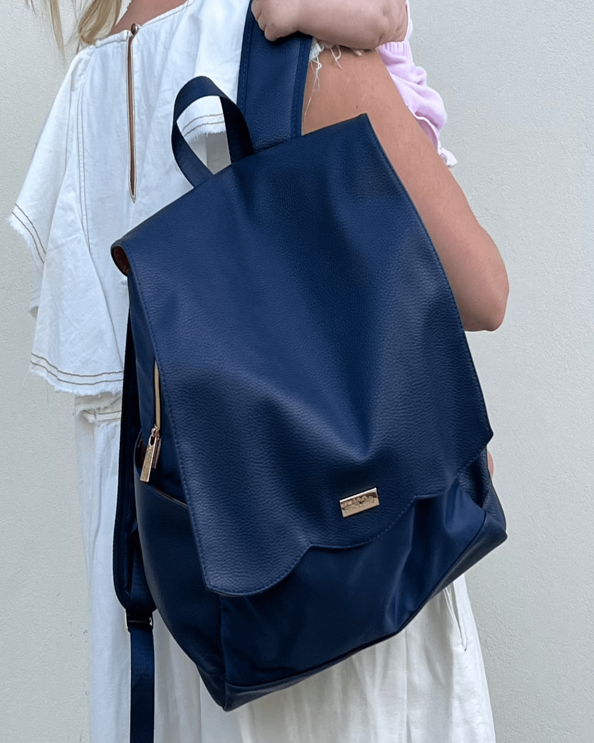 Close-up of navy diaper bag backpack with front flap pocket and gold logo plate