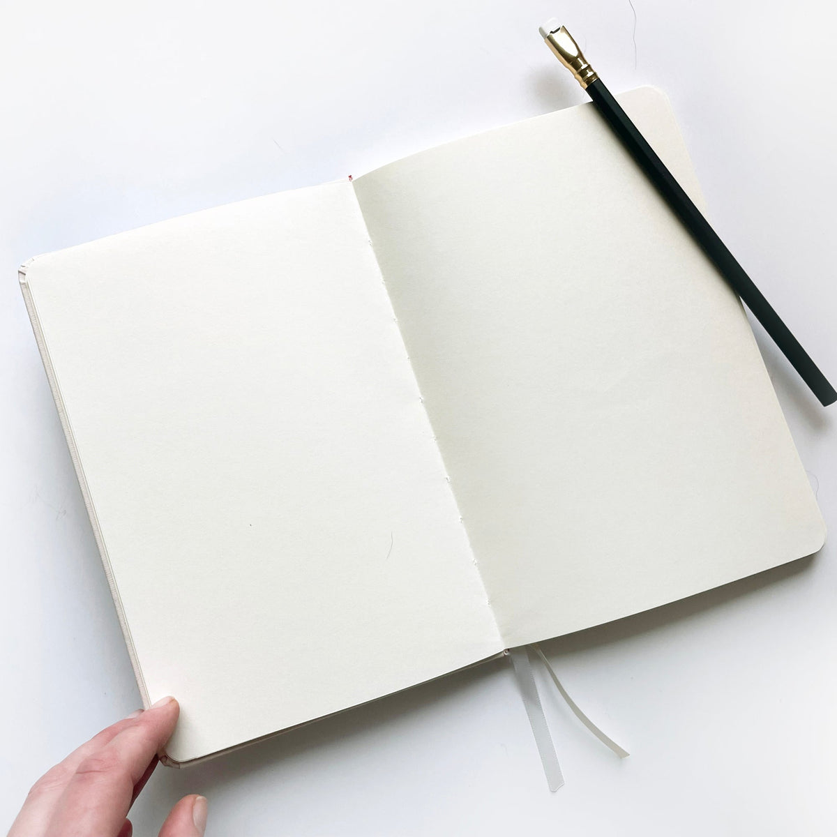 Open pink notebook with blank white pages and stitched binding