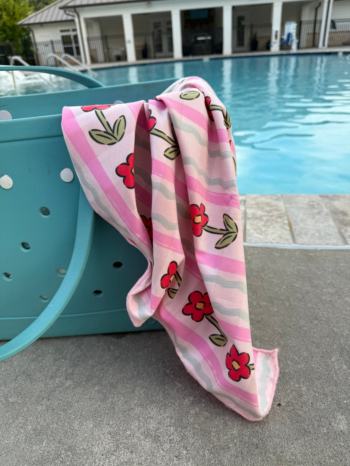 Pink quick-dry towel draped poolside with red flowers and green leaves