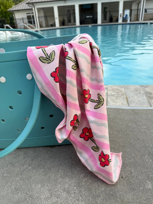 Pink quick-dry towel draped poolside with red flowers and green leaves