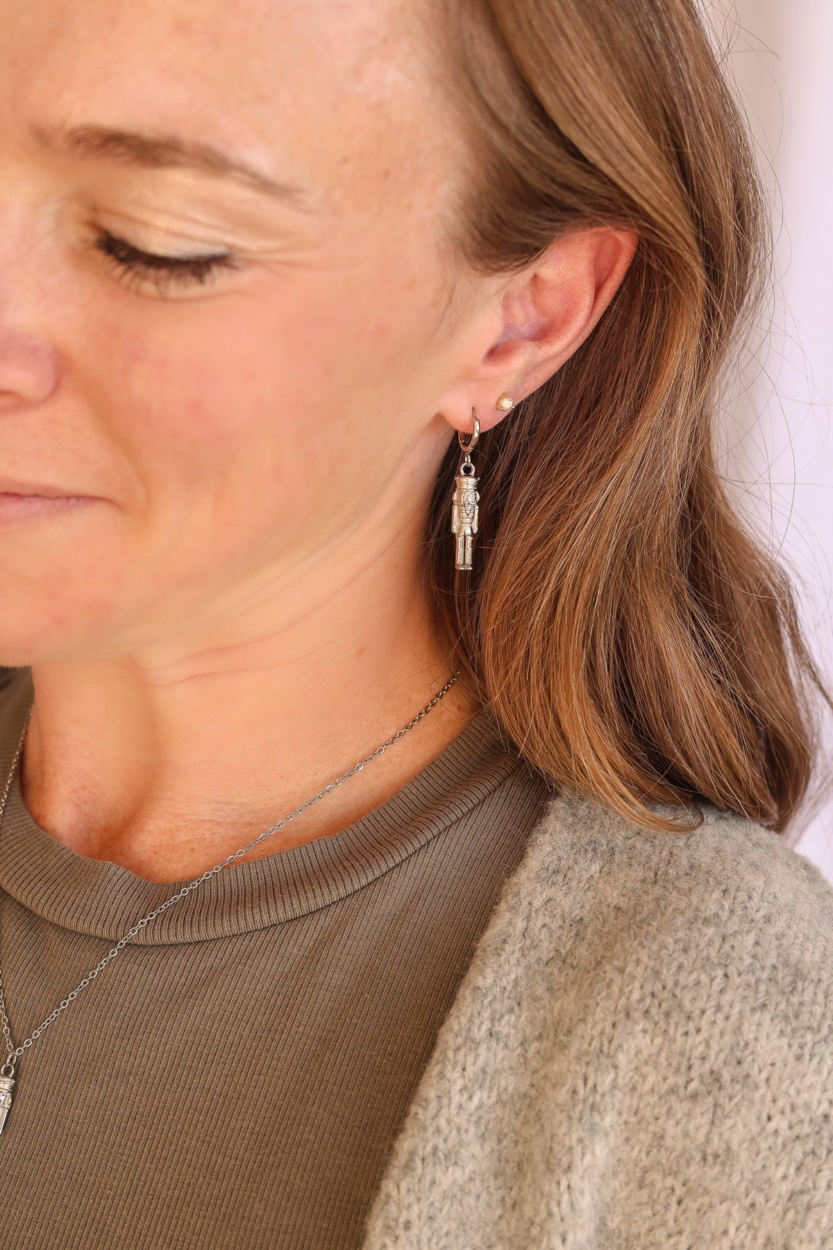 Silver nutcracker huggie hoop earring worn with a dangling soldier charm